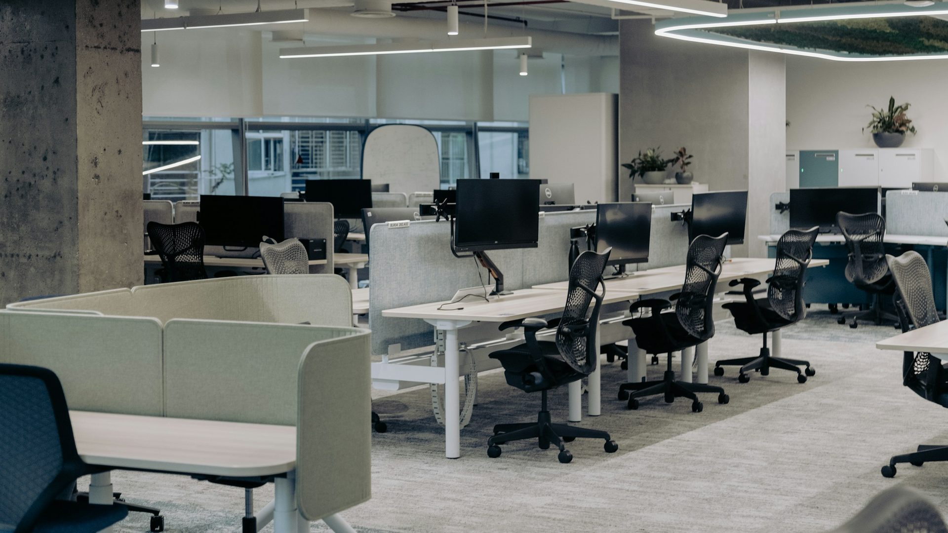 A finished open-plan office install — rows of benching workstations with fabric privacy screens, ergonomic task chairs, and monitor arms